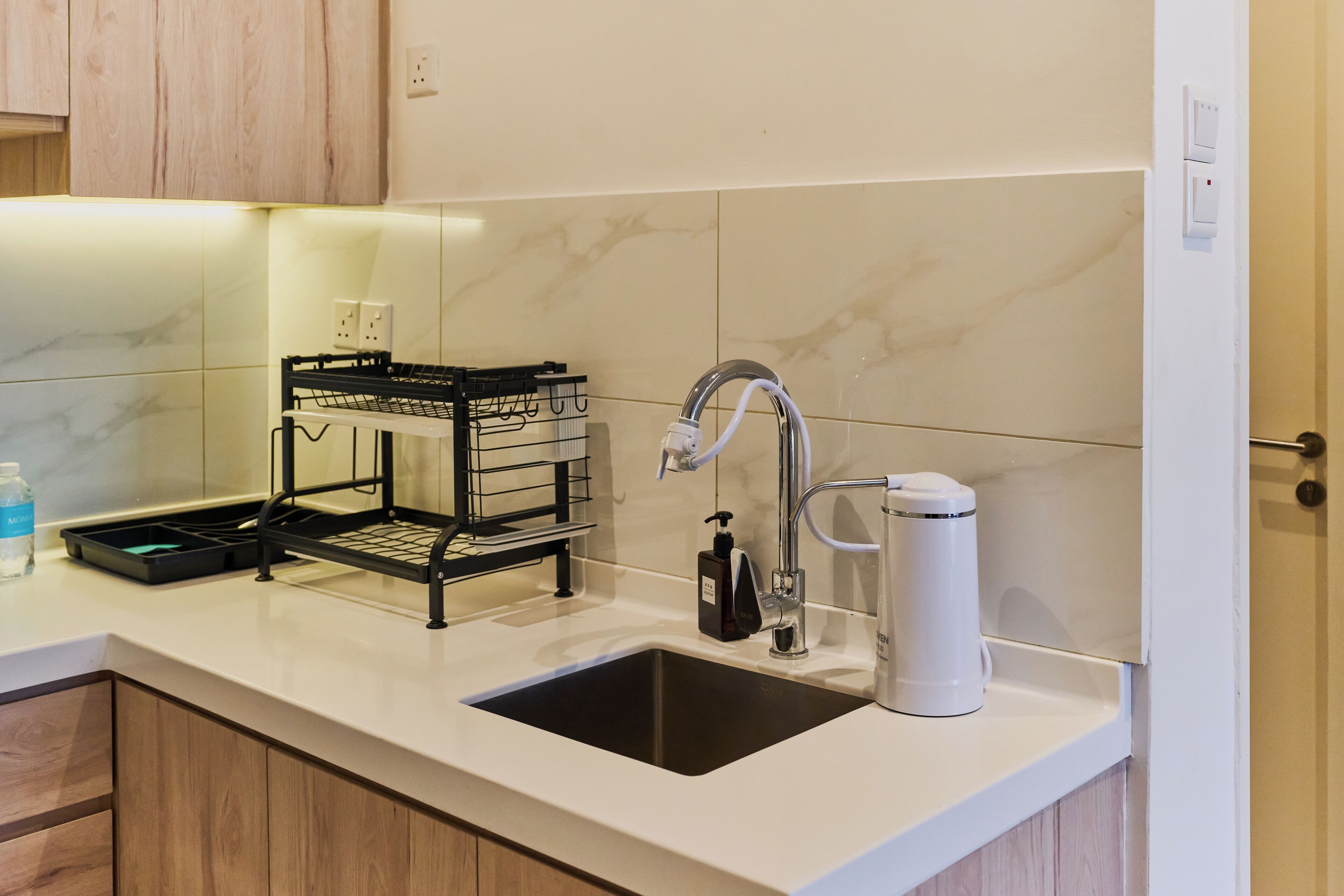 A modern kitchen with a white countertop, a black sink, a coffee maker, and a soap dispenser.
