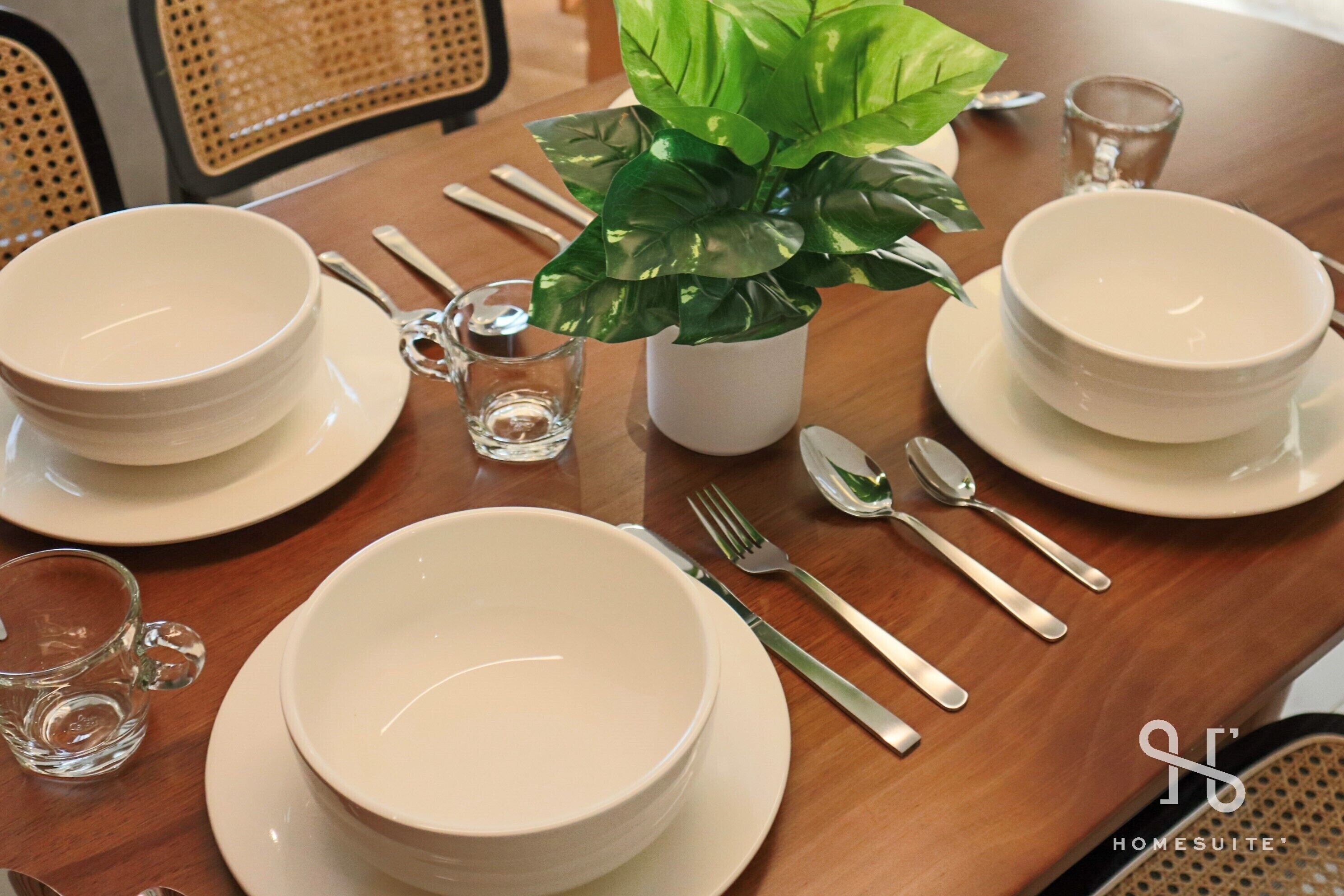 A dining table set with white plates, bowls, and cutlery, including a glass of water and a small glass pitcher.