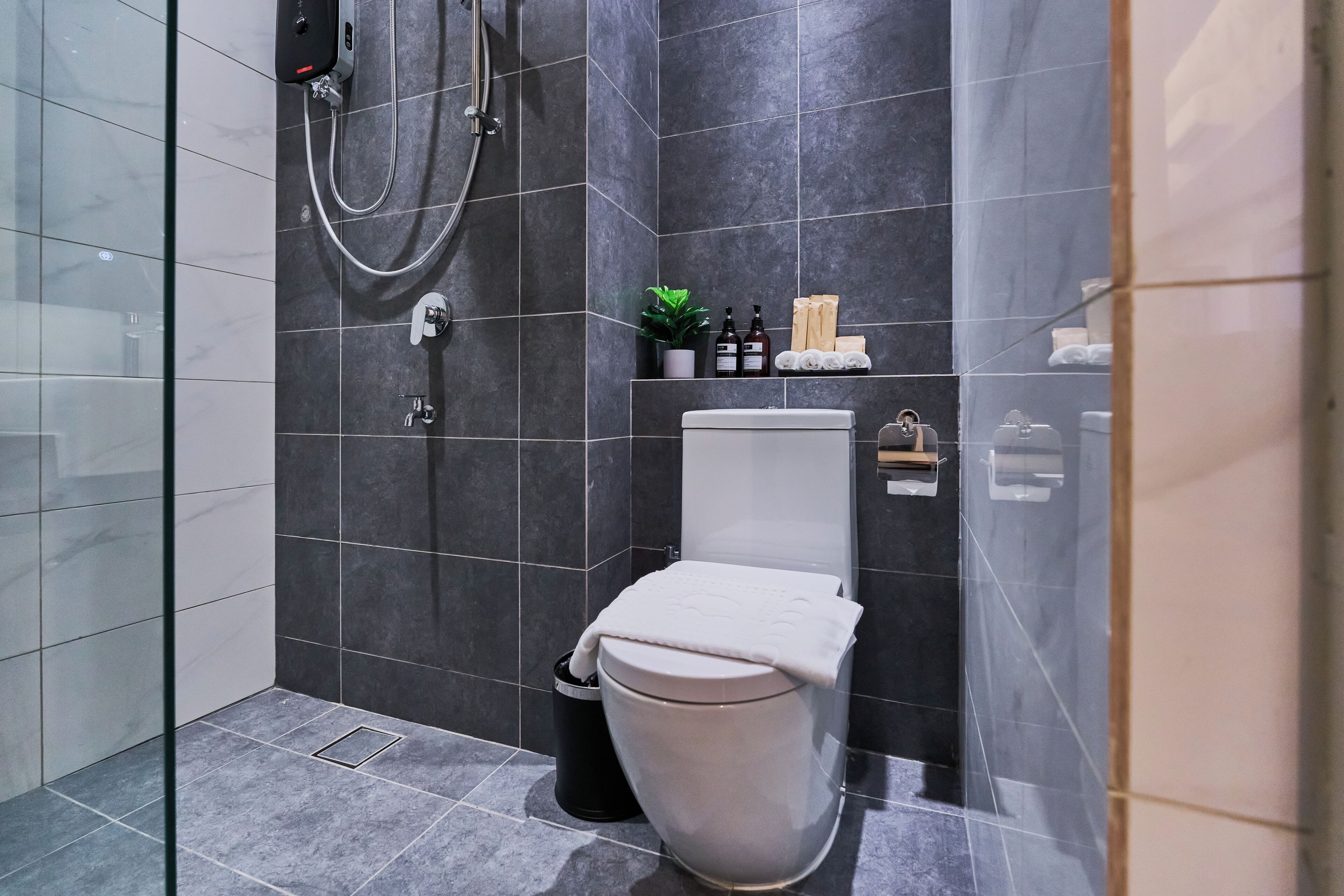 Un baño moderno con ducha de vidrio, inodoro y repisa con artículos de aseo.