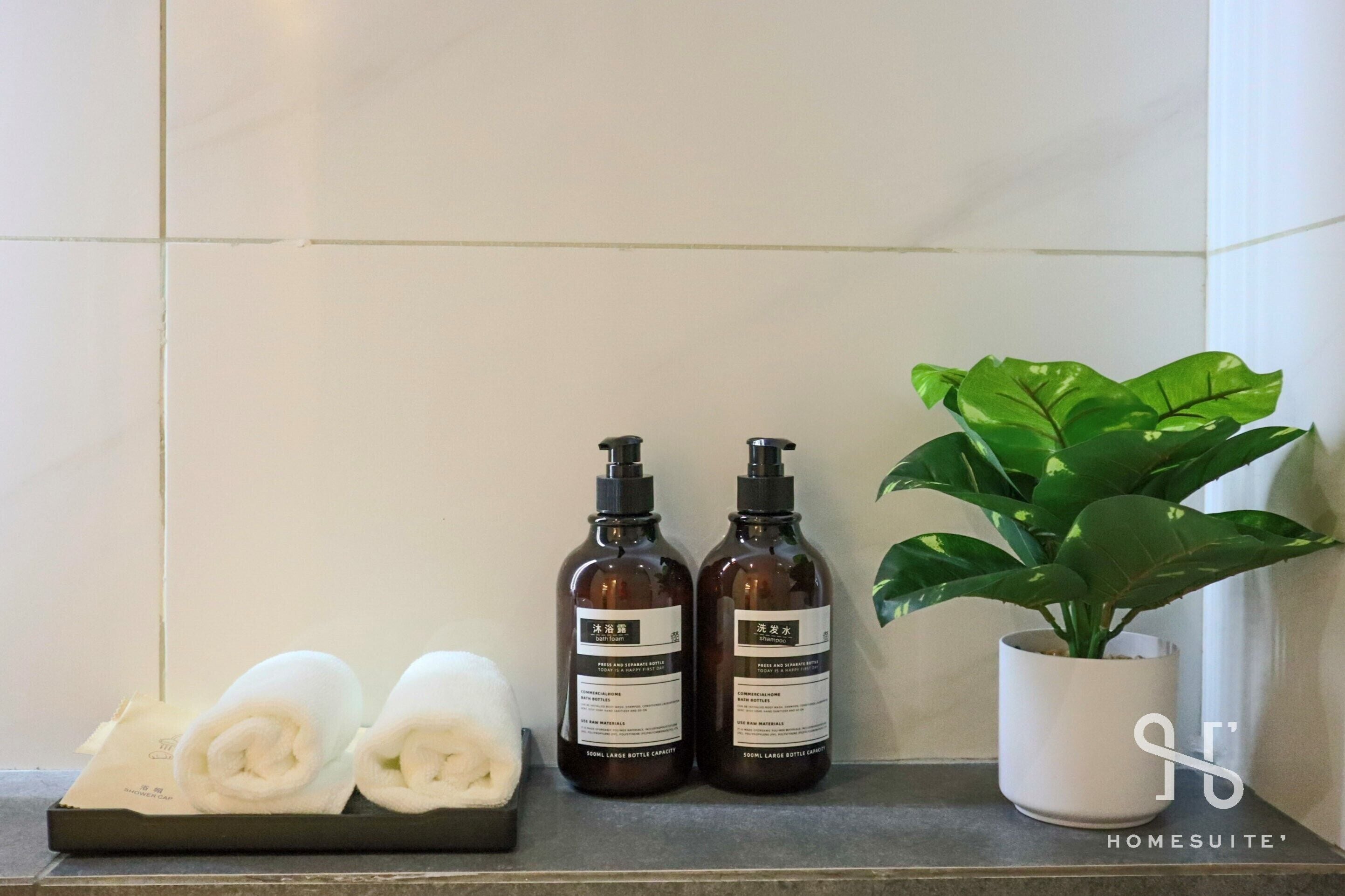 A bathroom with two bottles of shampoo, two rolled towels, and a potted plant.