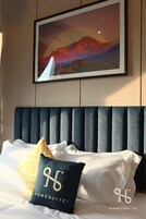 Una habitación de hotel con una cama, un cuadro enmarcado de un paisaje montañoso y un cabecero.