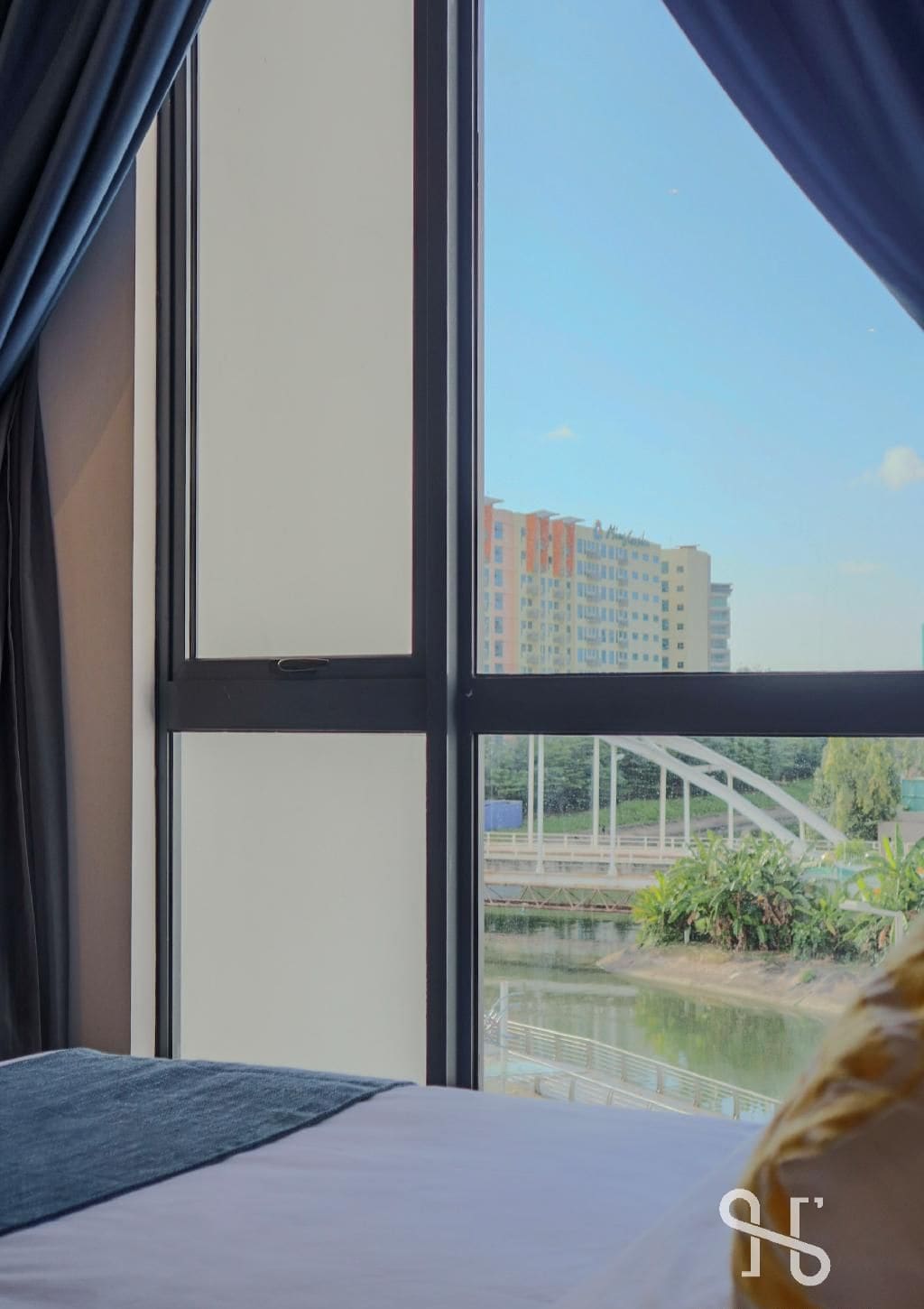 A hotel room with a large window offering a view of a bridge and buildings.