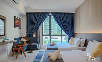 Habitación de hotel con una cama grande, un sofá, un escritorio y una silla. Cuenta con una ventana con cortinas, un cuadro en la pared y vistas a edificios.