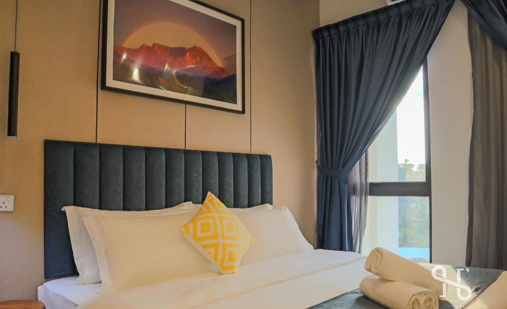 A hotel room with a bed, a painting on the wall, and a window with curtains.