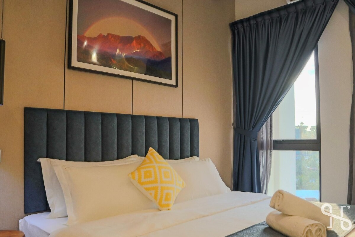 Una habitación de hotel con una cama, un cuadro en la pared y una ventana con cortinas.