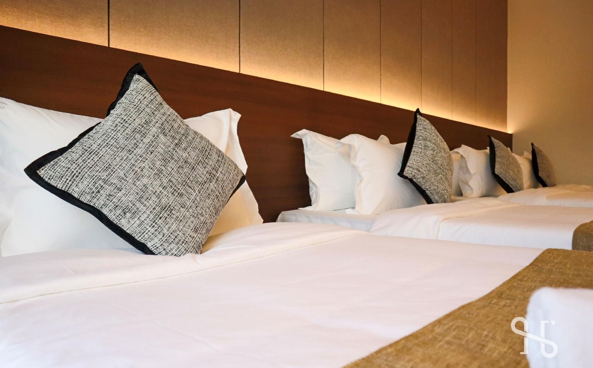 A hotel room with two beds, each with white linens and black-trimmed pillows.
