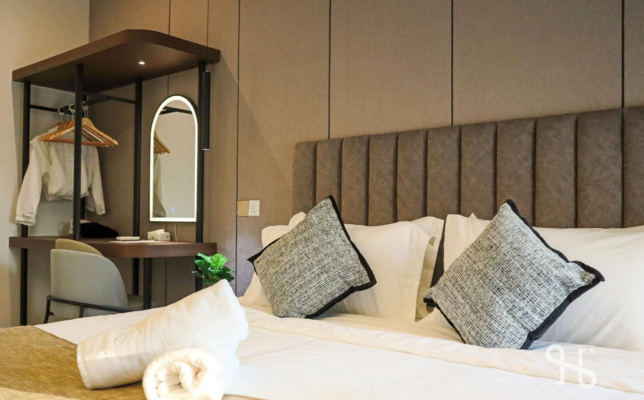 A hotel room with a bed, a desk, a chair, a hanging coat rack, and a mirror.