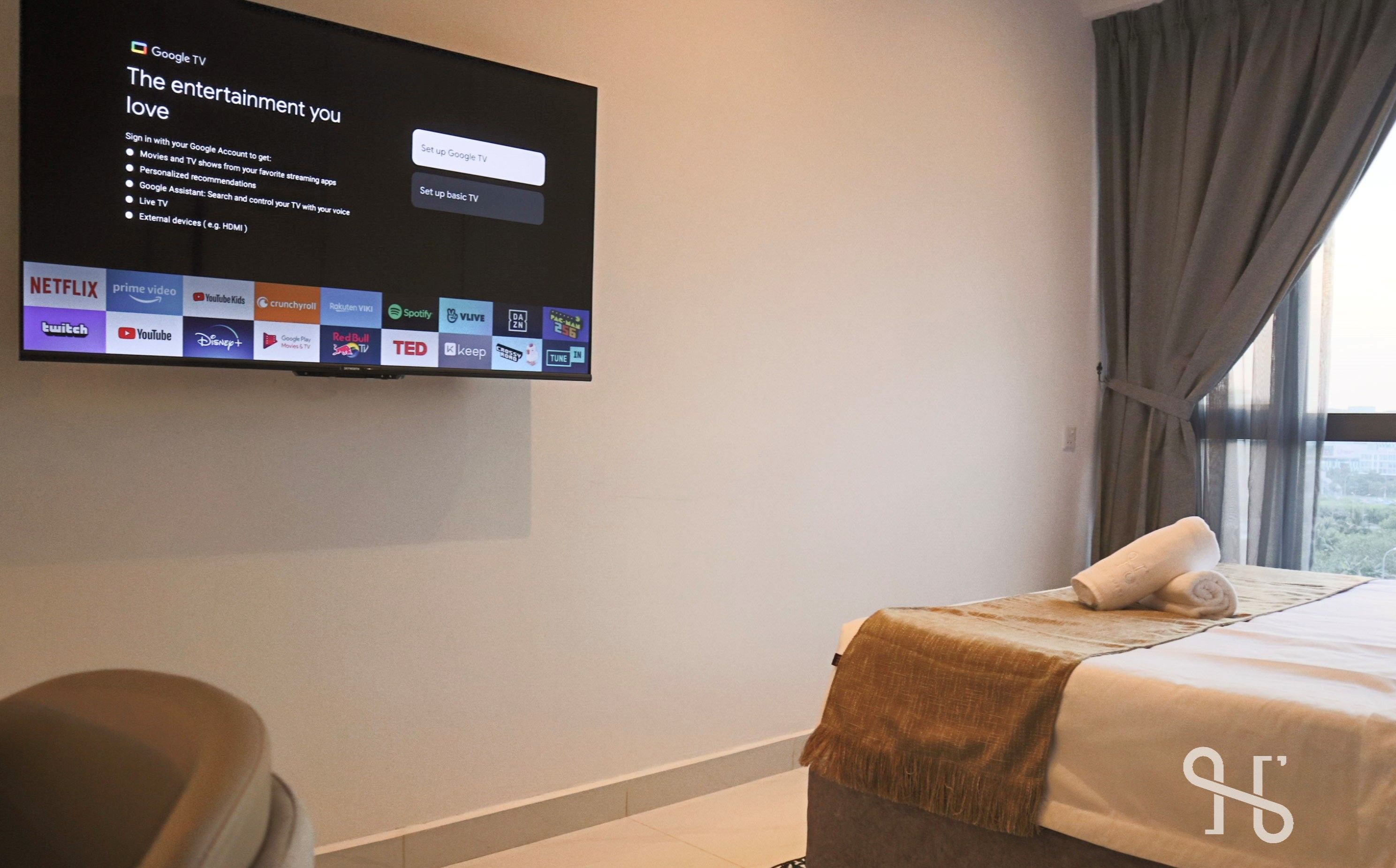 A hotel room with a flat-screen TV mounted on the wall displaying a Google TV interface.