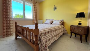 Ein Schlafzimmer mit einem hölzernen Bett, einem Nachttisch mit Lampe und einem Fenster mit Vorhängen.