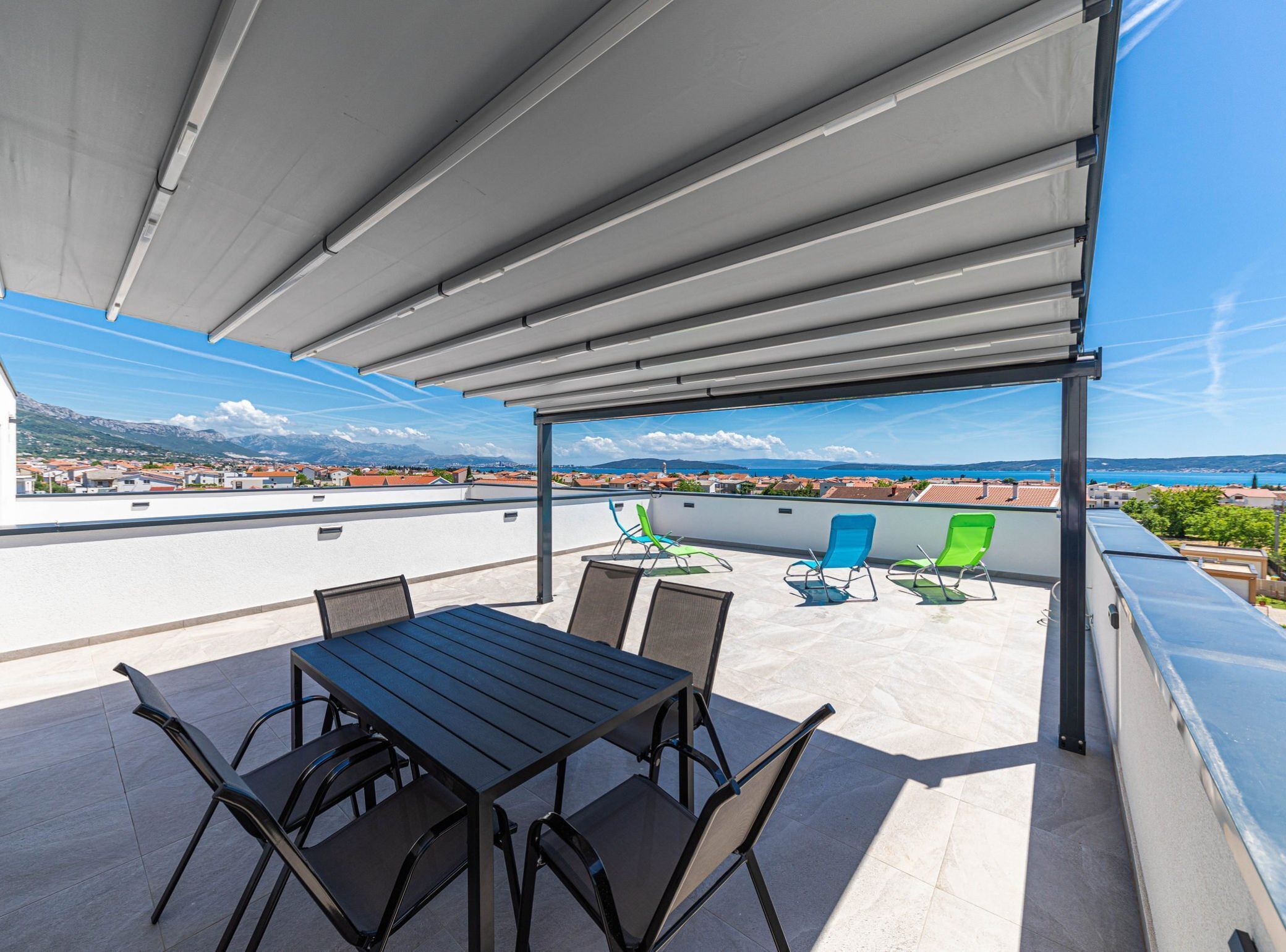 A rooftop terrace with a table and chairs, a covered area, and a view of a coastal town.