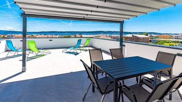 A rooftop terrace with a table and chairs, a pergola, and a view of the city and sea.