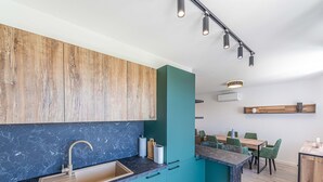 A modern kitchen with teal cabinets, a marble countertop, and a wooden backsplash.