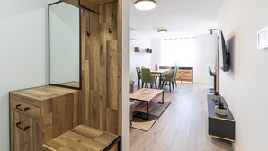 A modern interior with a wooden cabinet, a dining area with green chairs, and a TV mounted on the wall.