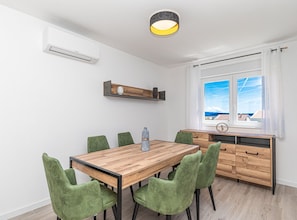Un comedor moderno con una mesa de madera y sillas tapizadas en verde, un banco empotrado con cajones, y una ventana con vistas al mar.