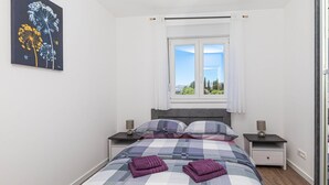 A bedroom with a bed, two bedside tables, a window with a view, and a painting on the wall.