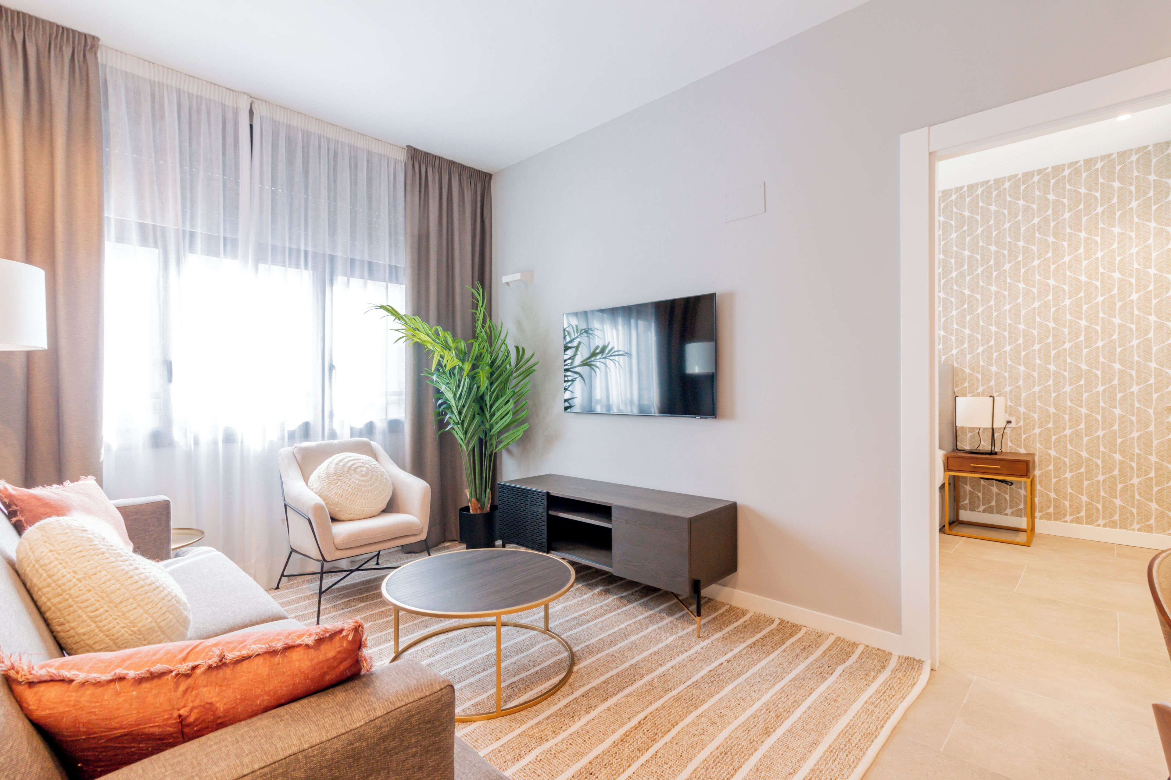 Una sala de estar moderna con sofá, sillón, mesa de centro y televisor en la pared.