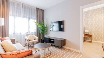 Una sala de estar moderna con sofá, sillón, mesa de centro y televisor en la pared.