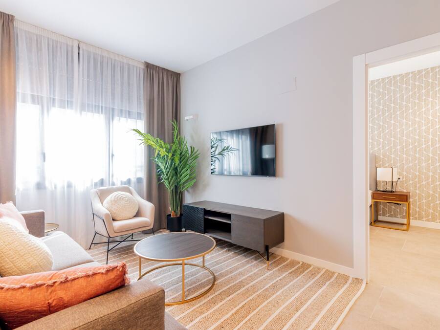 Una sala de estar moderna con sofá, sillón, mesa de centro y televisor en la pared.