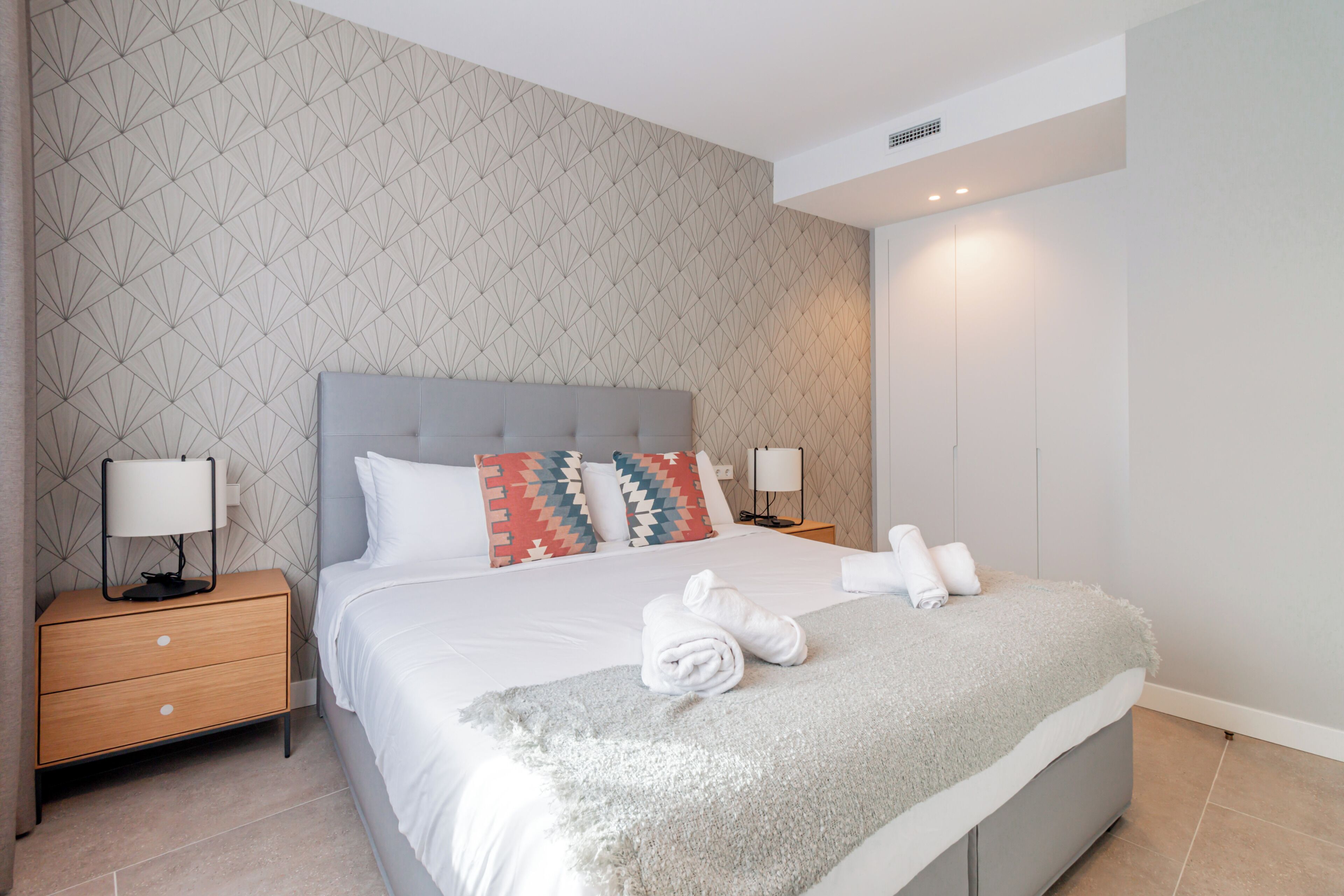 Een moderne hotelkamer met een groot bed, een nachtkastje met een lamp en een wand met een geometrisch patroon.