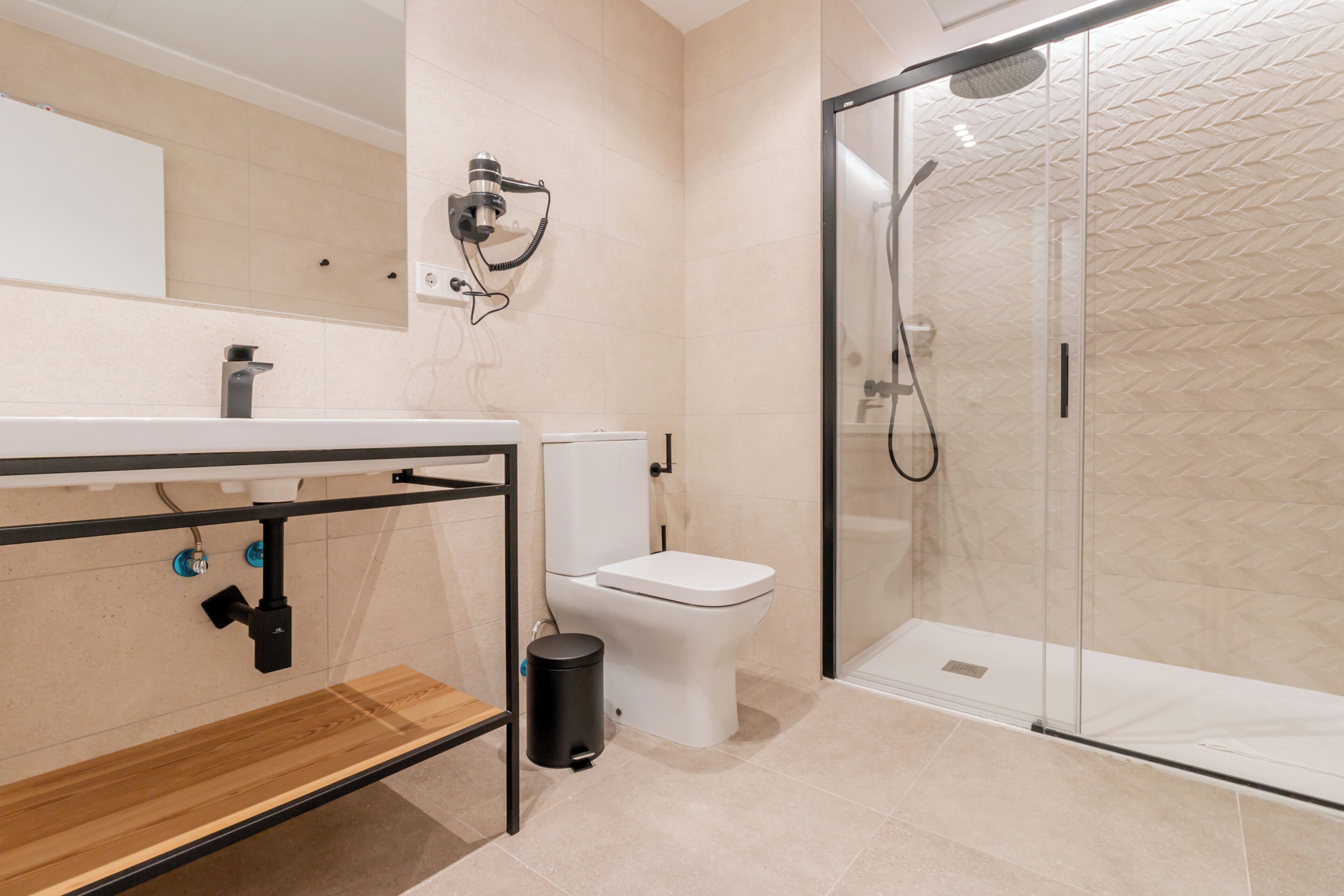A modern bathroom with a glass shower enclosure, a toilet, and a sink with a wooden shelf.