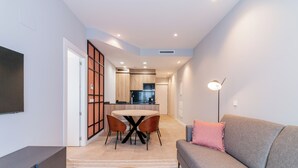 Een moderne woonkamer met een grijze bank, een ronde salontafel, en een eethoek met een ronde tafel en stoelen.