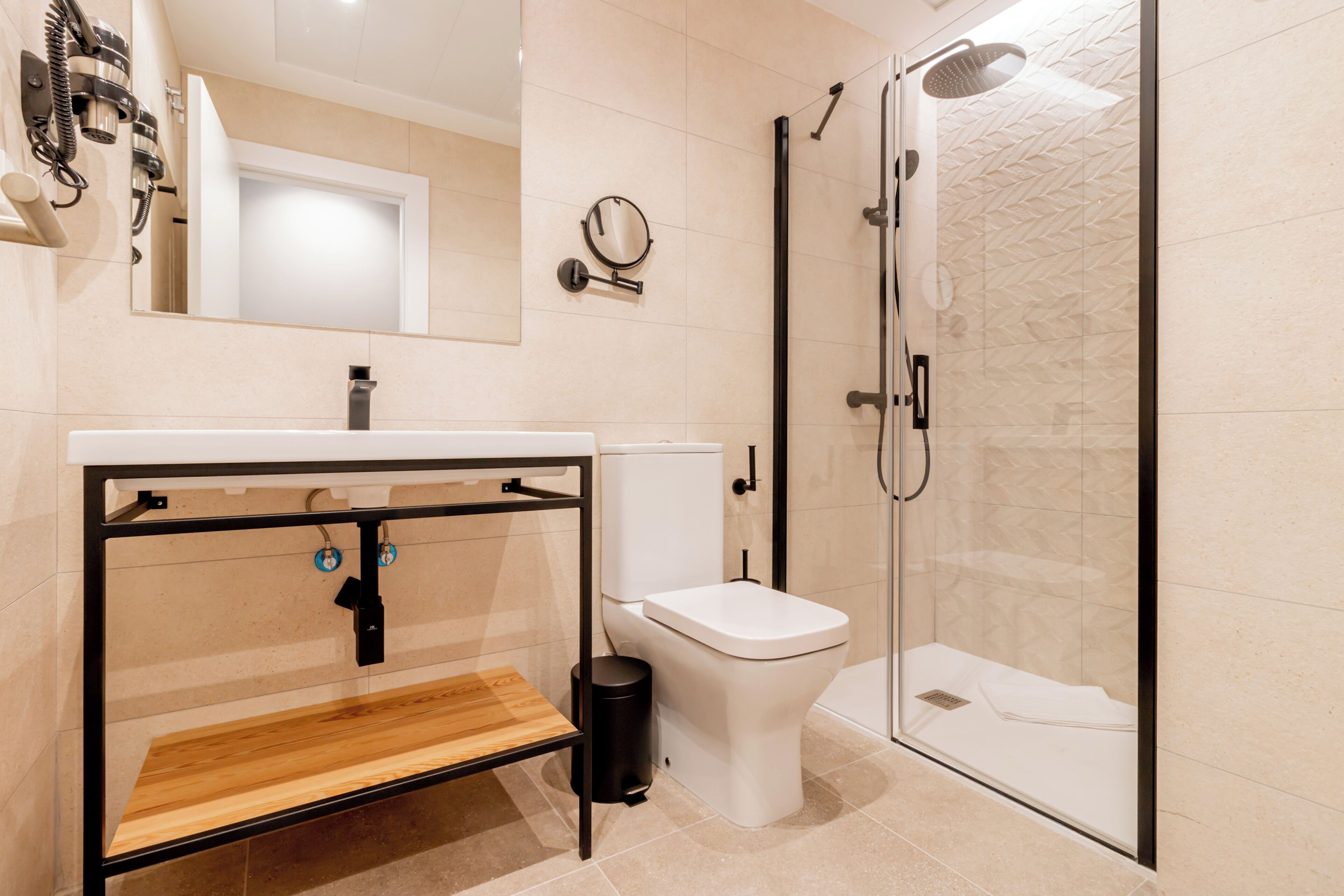 A modern bathroom with a wooden vanity, a toilet, a glass shower enclosure, and a mirror.