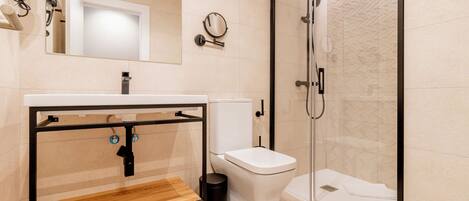 A modern bathroom with a wooden vanity, a toilet, a glass shower enclosure, and a mirror.