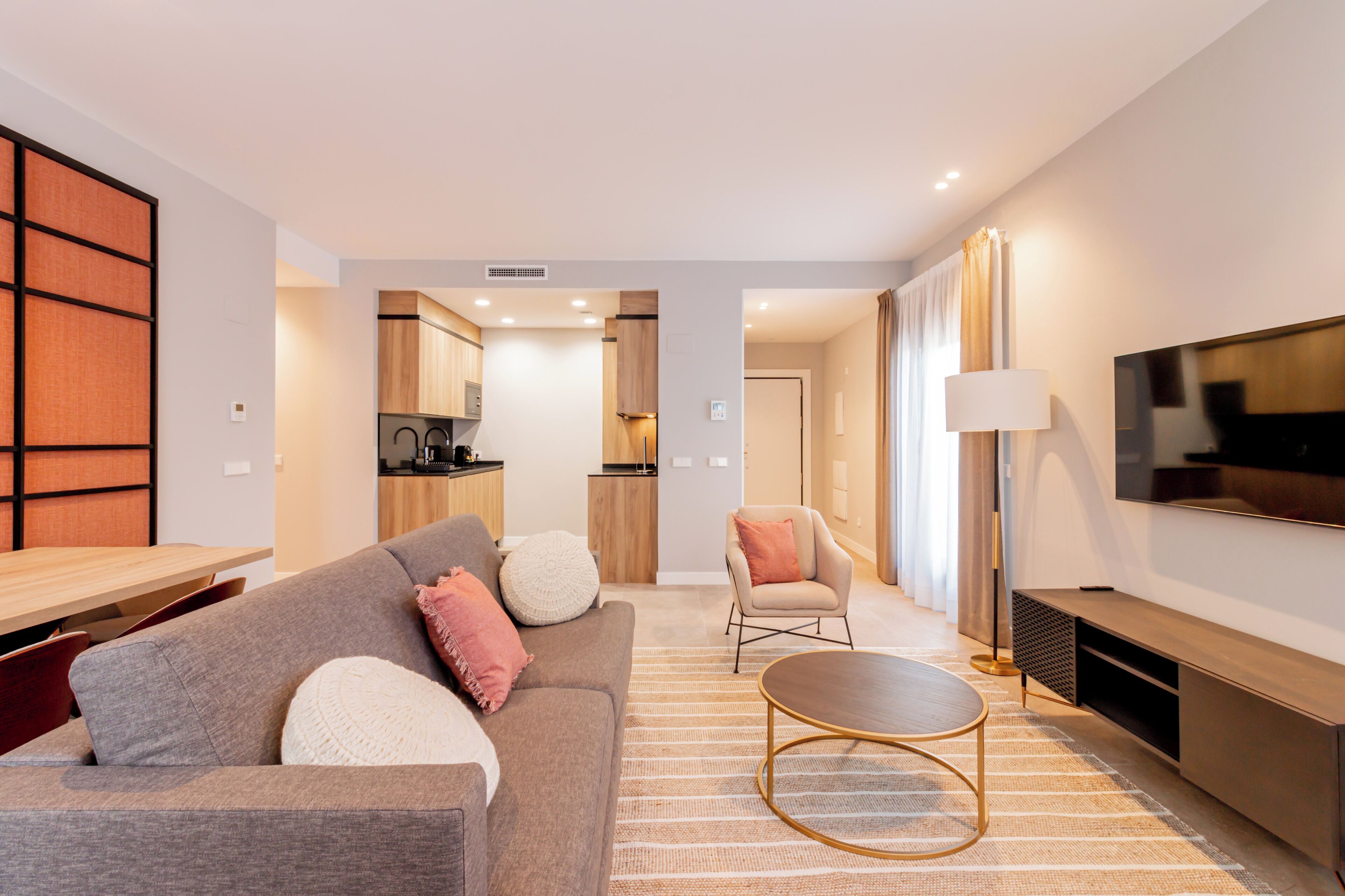 Una sala de estar moderna con un sofá, una mesa de centro y un televisor. Se ve una cocina al fondo.