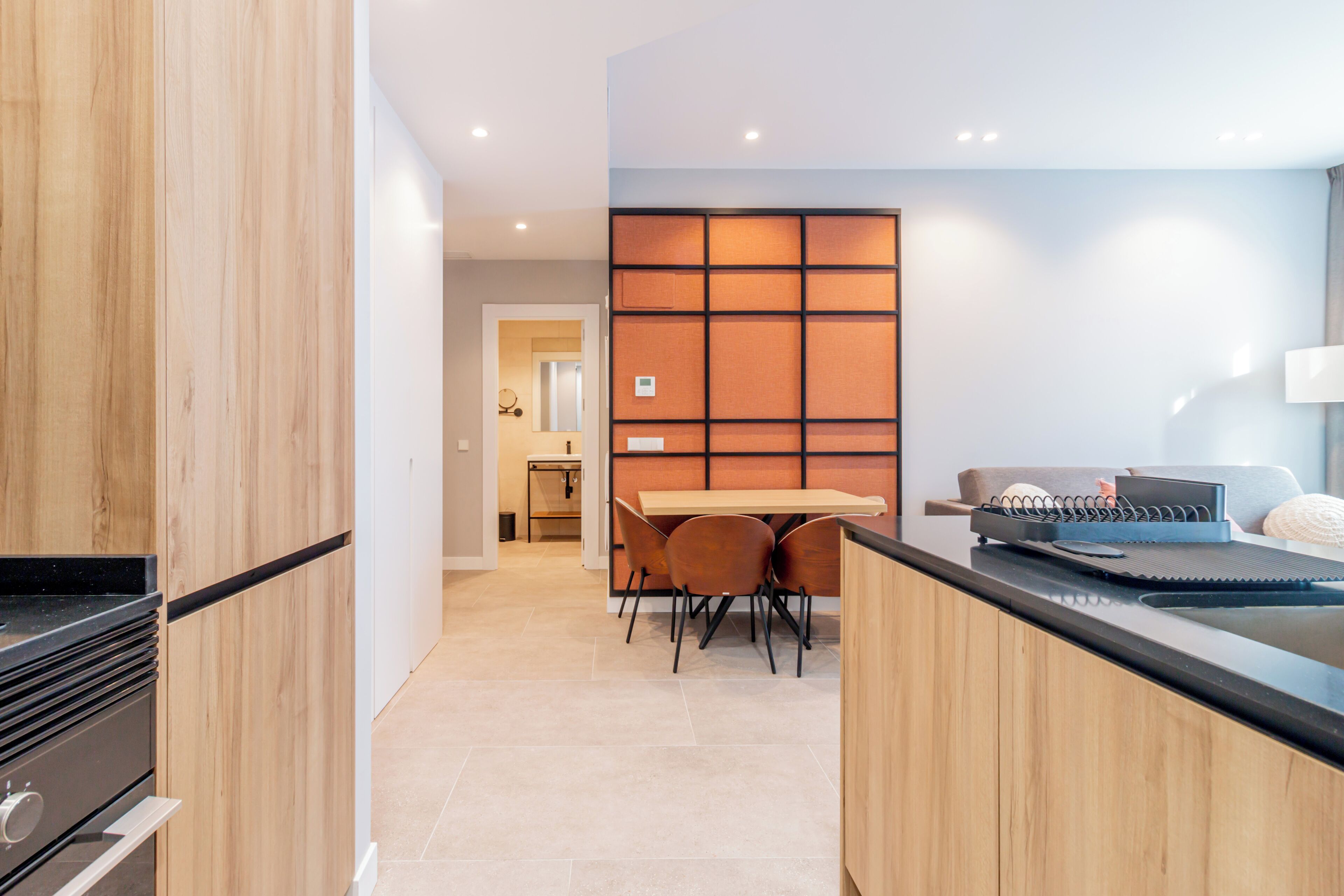A modern kitchen with wooden cabinets, a black countertop, and a dining area with a table and chairs.
