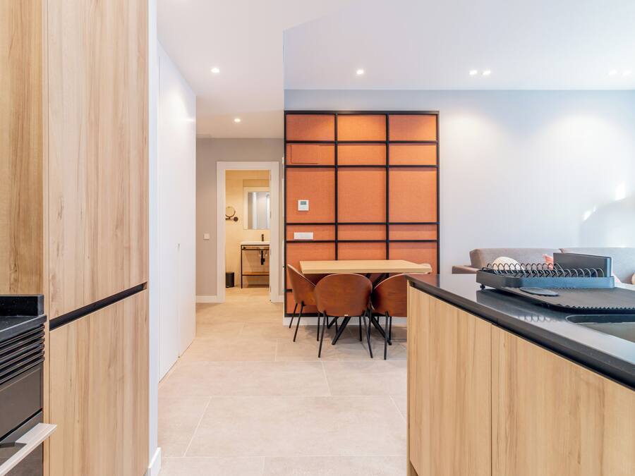A modern kitchen with wooden cabinets, a black countertop, and a dining area with a table and chairs.