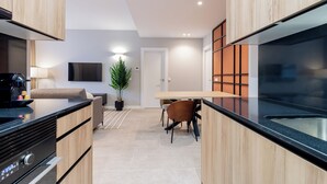 Een moderne keuken met houten kastjes, een zwart aanrecht en een ingebouwde kookplaat. Er is een eethoek met een tafel en stoelen, en een potplant in de hoek.