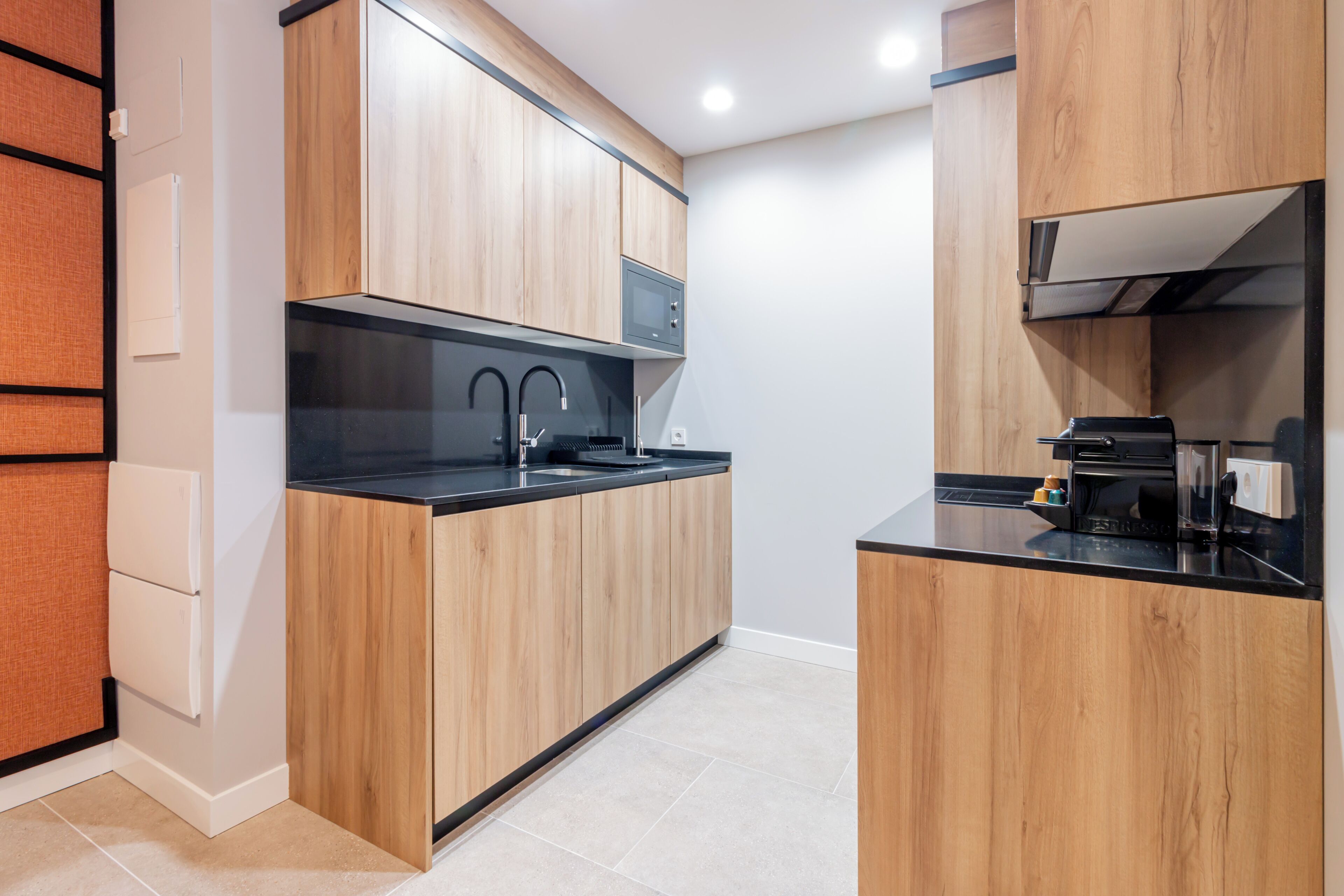 A modern kitchen with wooden cabinets, a black countertop, and a built-in microwave.