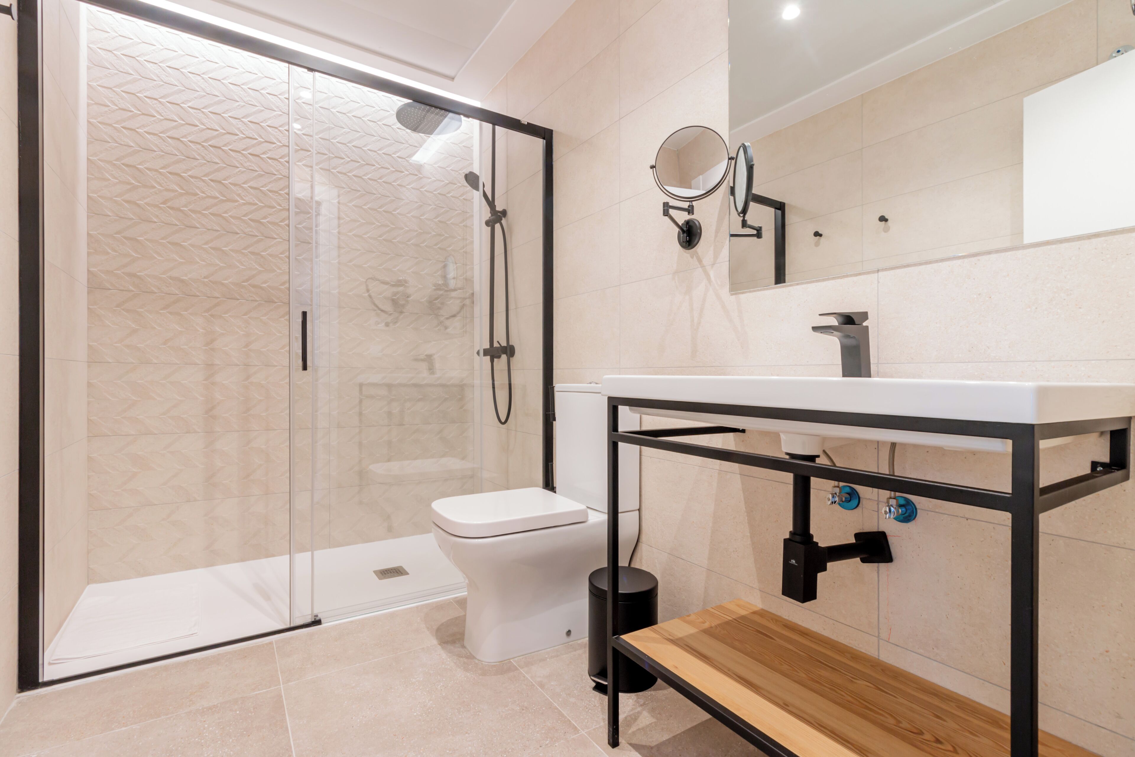 A modern bathroom with a glass-enclosed shower, a white toilet, and a wooden vanity with a mirror.