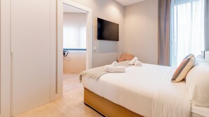 Een hotelkamer met een bed, een aan de muur bevestigde televisie en een badkamer die door een geopende deur zichtbaar is.