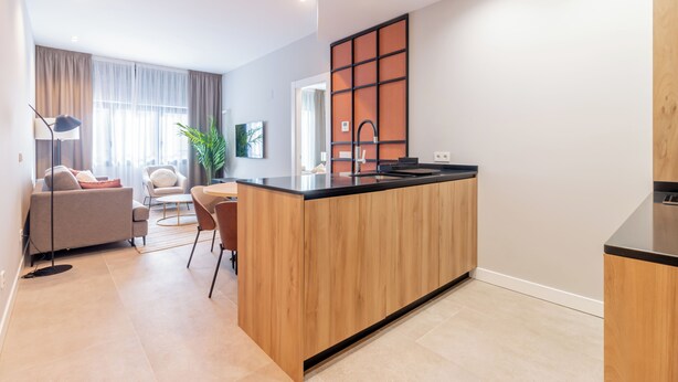 Een moderne keuken met een centraal eiland, een eetgedeelte met een ronde tafel en stoelen, en een zithoek met een bank en een lamp.