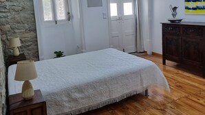 A bedroom with a bed, wooden flooring, a stone wall, a wooden ceiling, and a door. - Casa da Ti Alzira - a refuge at the foot of the mountain with a touch of tradition (Leiria)