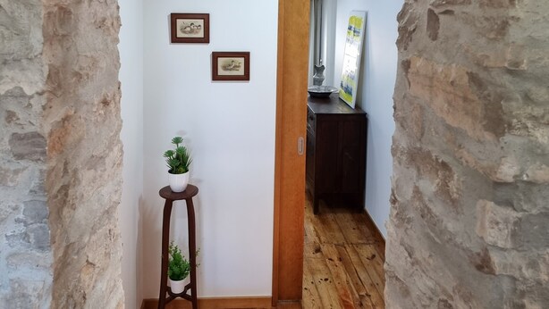 A narrow hallway with stone walls, wooden flooring, and a small wooden stool with a plant. - Casa da Ti Alzira - a refuge at the foot of the mountain with a touch of tradition (Leiria)