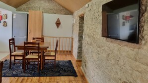 A dining area with a wooden table and chairs, a stone wall, and a mounted TV. - Casa da Ti Alzira - a refuge at the foot of the mountain with a touch of tradition (Leiria)