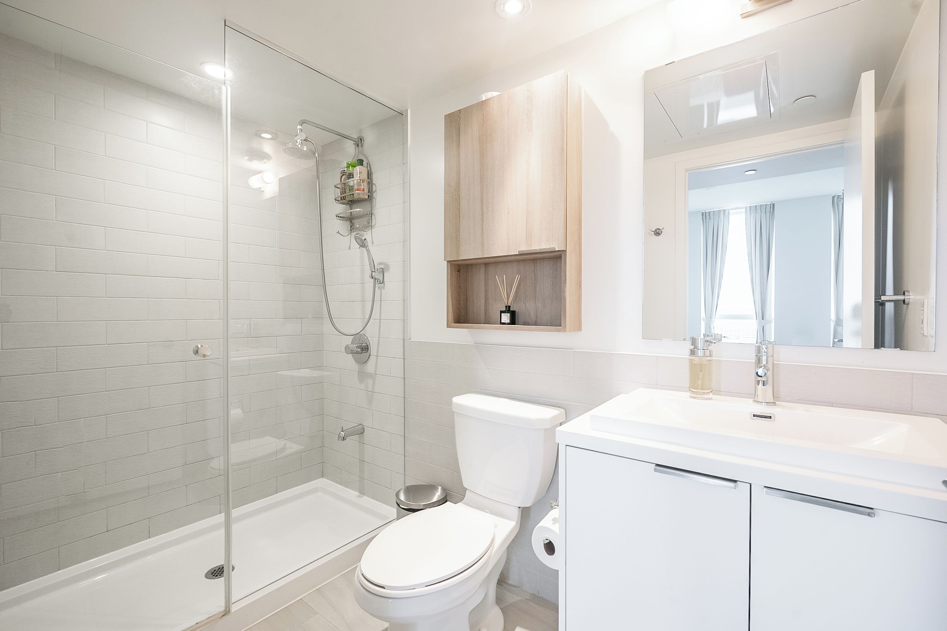 A modern bathroom with a glass-enclosed shower, a white toilet, and a sink with a mirror above it.