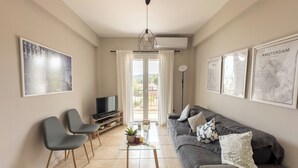 A living room with a sofa, chairs, a TV, a coffee table with a plant, and a balcony with curtains.