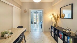 A modern kitchen with a dining area, a hallway leading to a balcony, and a bookshelf with books and decorative items.