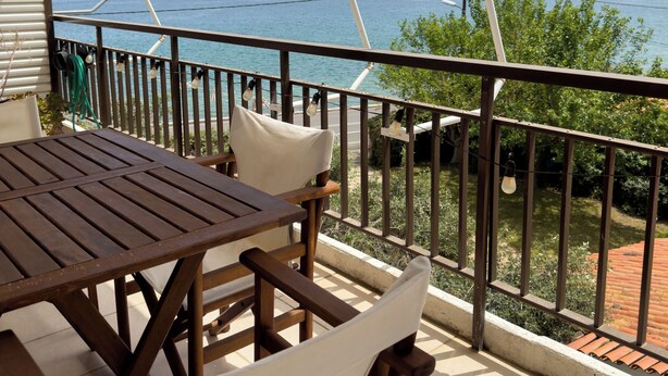 A wooden table and chairs on a balcony with a view of the sea and distant mountains.