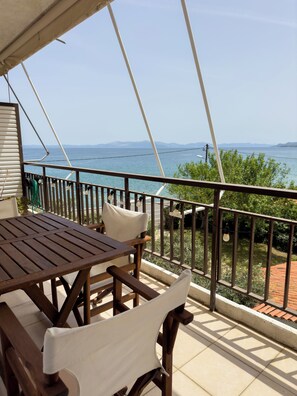 A wooden table and chairs on a balcony with a view of the sea and distant mountains.