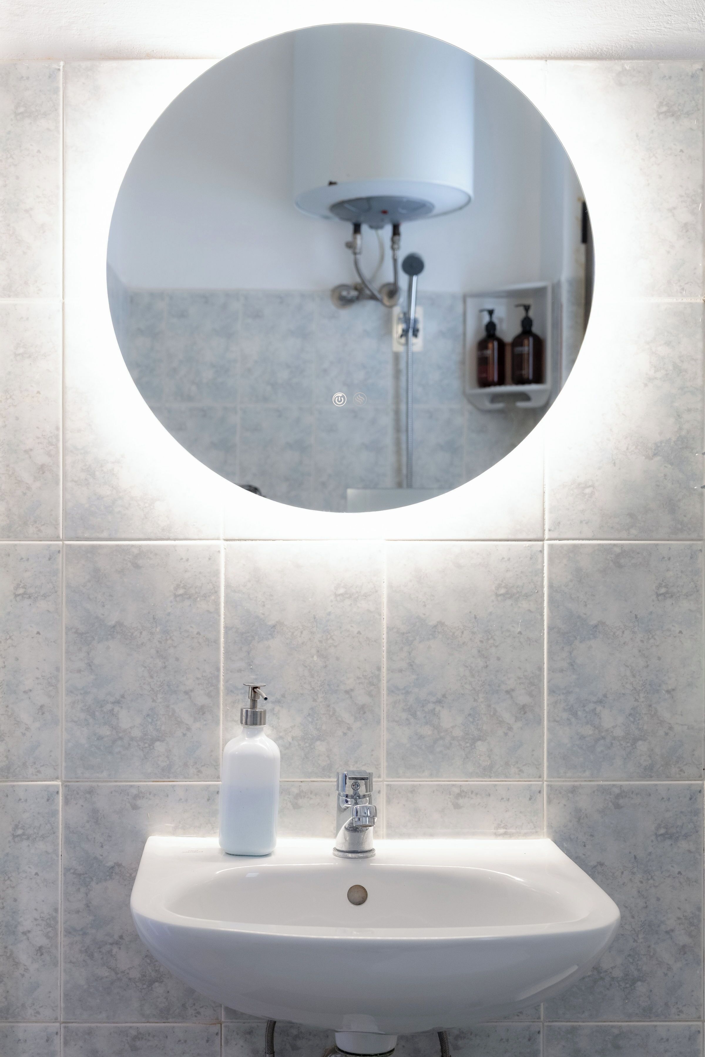 Un baño con un espejo redondo, un lavamanos y un cabezal de ducha.