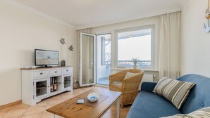 A living room with a television, a sofa, a coffee table, and a wicker chair. - WindSpiel - House Ankerlicht - Westerland (Westerland)