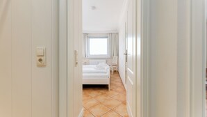 A hotel room with a bed, a chair, a window with curtains, and a tiled floor. - WindSpiel - House Ankerlicht - Westerland (Westerland)