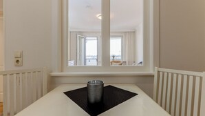 A hotel room with a large window, a table with a black placemat, and a white chair. - WindSpiel - House Ankerlicht - Westerland (Westerland)