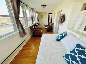 A bedroom with a large bed, two chairs, a mirror, and a window with curtains. - The Vintage Inn - Hidden Gem! (Redwood Falls)