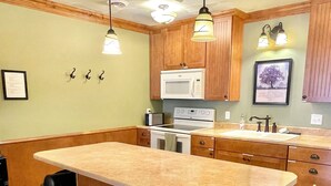 A kitchen with wooden cabinets, a large island with stools, a microwave, stove, and a sink. - The Vintage Inn - Hidden Gem! (Redwood Falls)