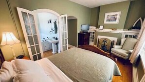A bedroom with a bed, a chair, a television, and a bathroom visible through an open door. - The Vintage Inn - Hidden Gem! (Redwood Falls)